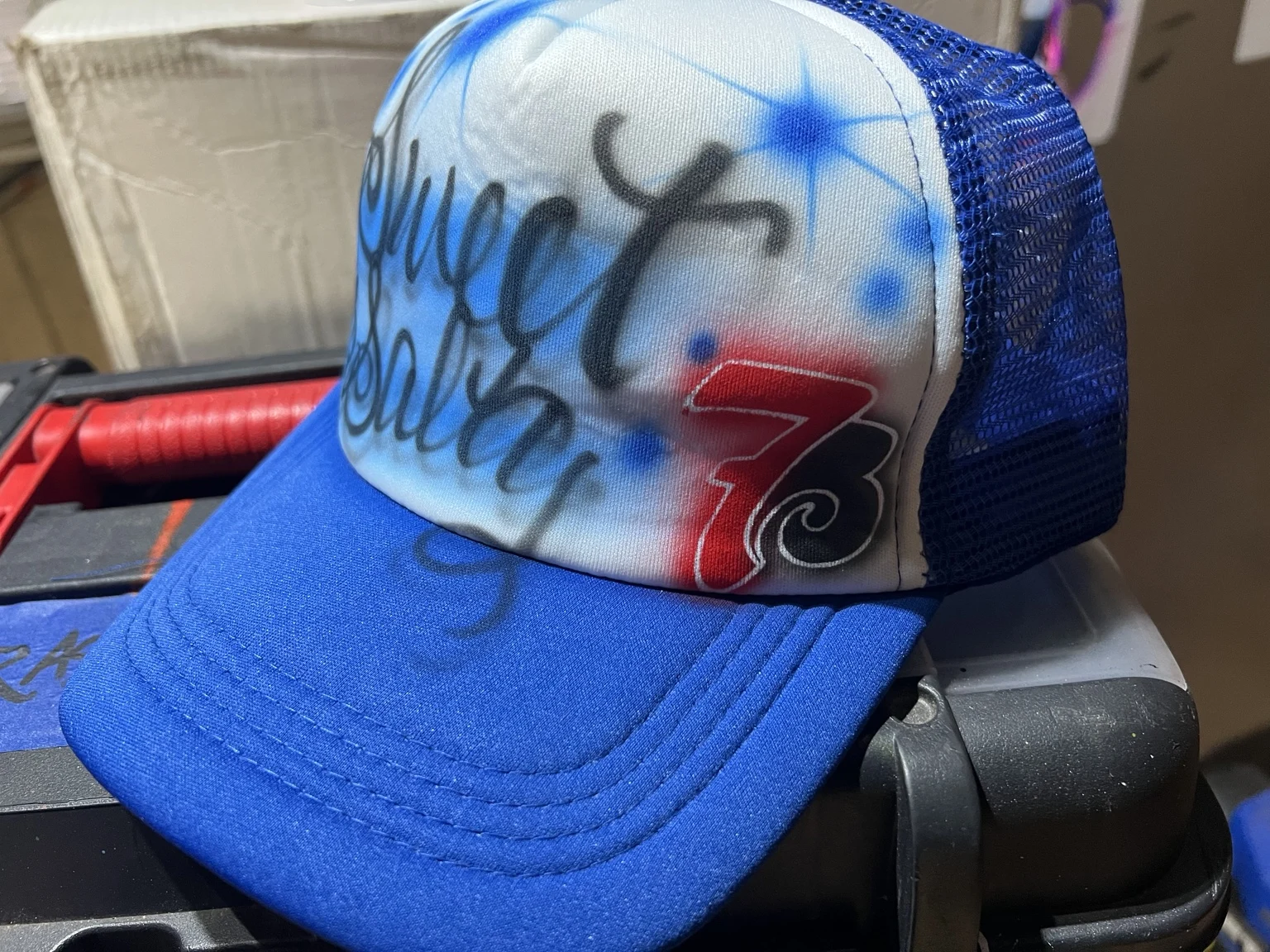Side view of a blue custom airbrush trucker hat with 7 Brew artwork for the Nashville event
