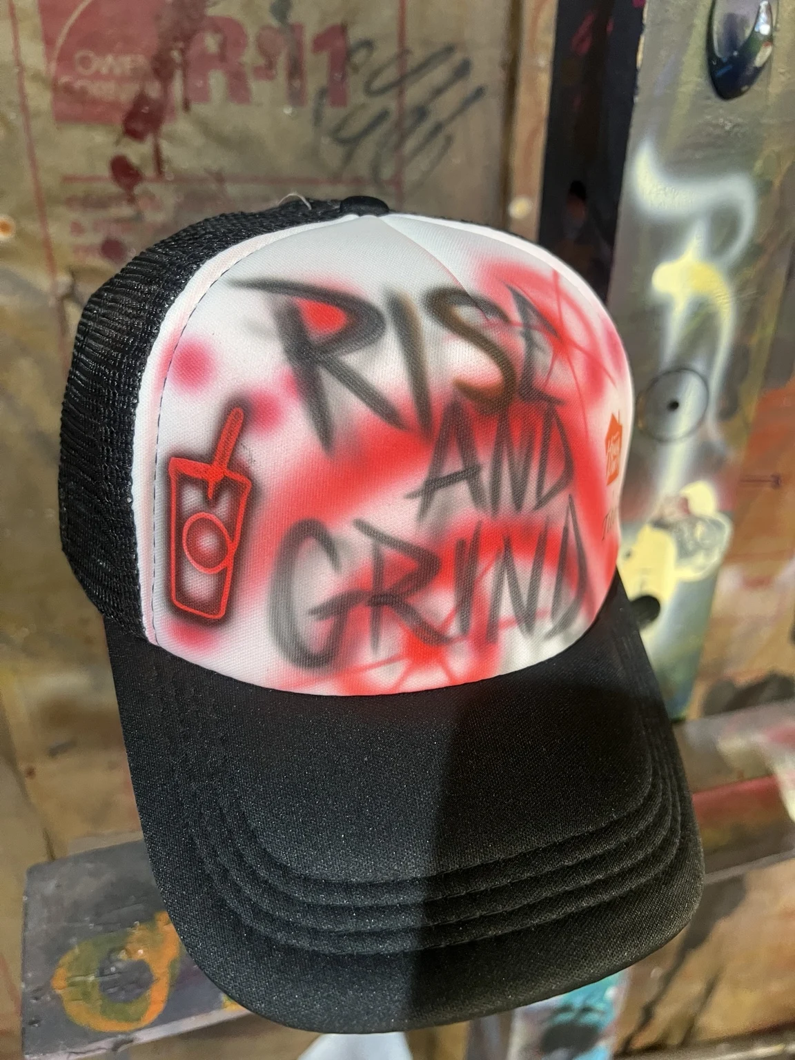Black trucker hat with Rise and Grind lettering and a red coffee cup design for 7 Brew in Nashville