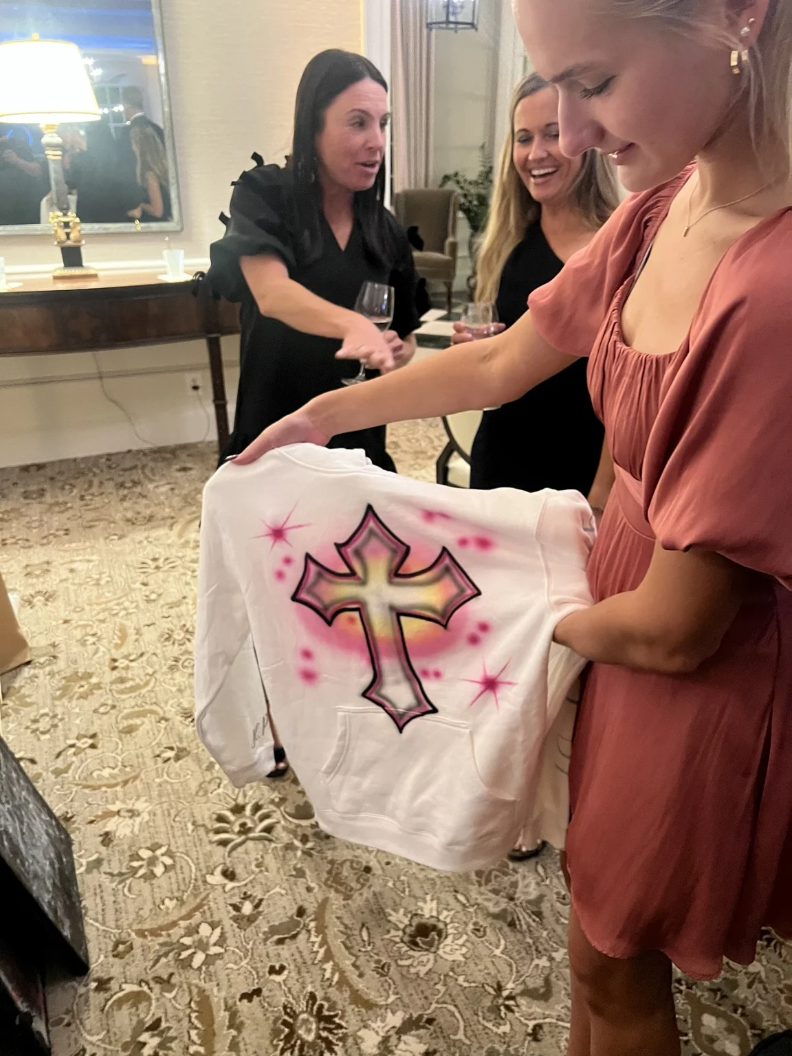 Guest holding a white shirt with a pink airbrushed cross design at the Monroe event